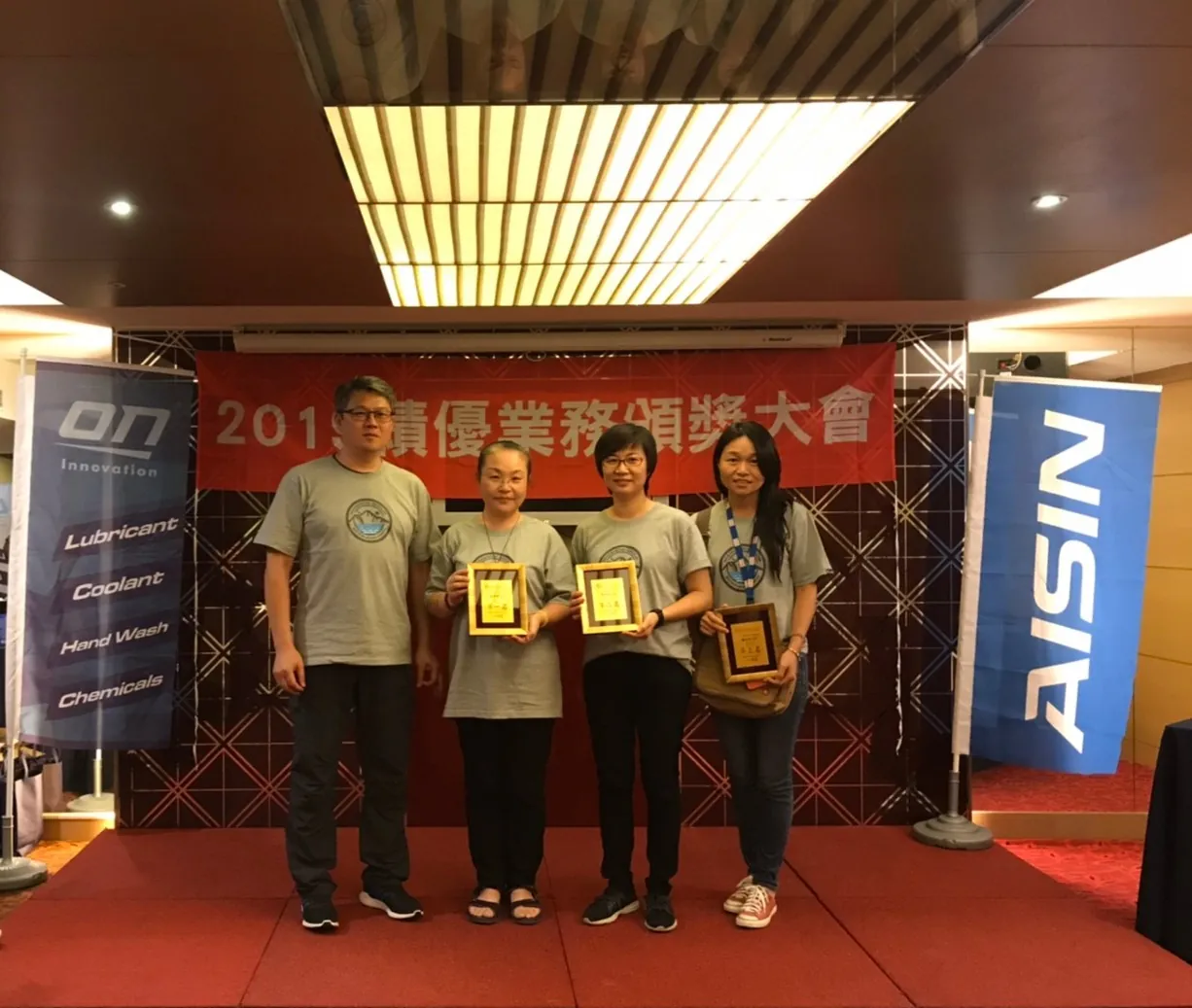 績優業務頒獎,得獎者手持獎牌站在 ON 與 AISIN 旗幟前